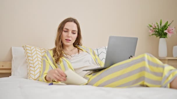 Mujer rubia joven usando portátil de lectura portátil en el dormitorio - Imágenes, Vídeo