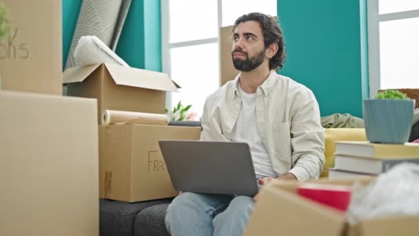 Fiatal spanyol férfi használ laptop ül a kanapén, amelynek ötlete az új otthon - Felvétel, videó