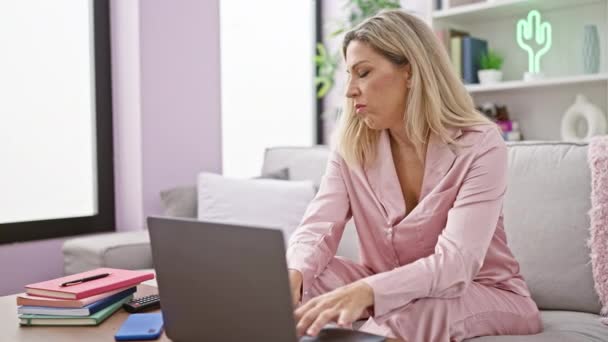 Mladá blondýna žena zavírání notebook s vážnou tváří ležící na pohovce krycí tvář s polštářem doma - Záběry, video