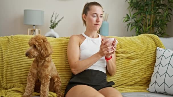 Mladá kavkazská žena se psem čichajícím šálek kávy sedí doma na pohovce - Záběry, video