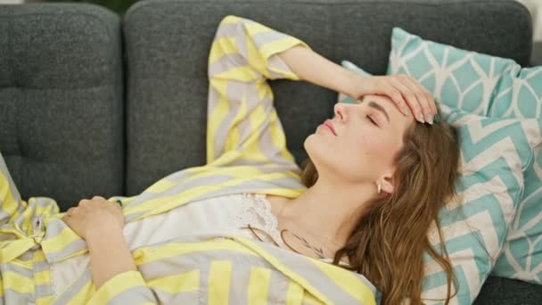 Nuori blondi nainen makaa sohvalla kärsimystä päänsärky kotona - Materiaali, video