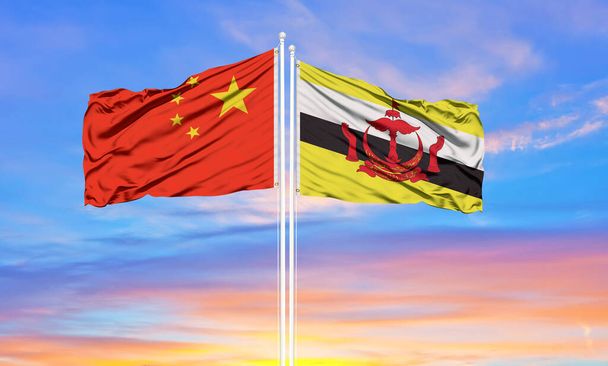 Bandera de China y Brunei ondeando en el viento contra el blanco cielo azul nublado juntos. Concepto diplomático, relaciones internacionales - Foto, imagen