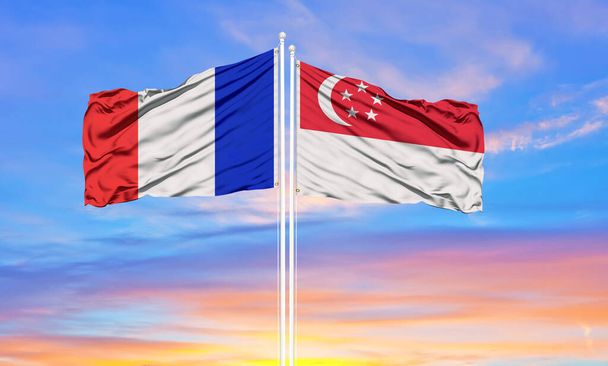 Γαλλία και τη Σιγκαπούρη δύο σημαίες σε κοντάρια σημαία και μπλε συννεφιασμένο ουρανό. Διπλωματία, διεθνείς σχέσεις - Φωτογραφία, εικόνα