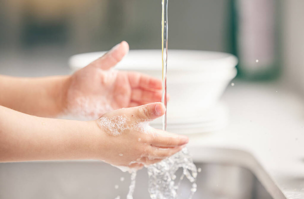 Dziecko, mycie rąk i kuchni z pianką w zbliżeniu dla zdrowia, bezpieczeństwa i zatrzymać bakterie w domu. Dziecko, czyszczenie dłoni i mydła wodą, płynem lub nauką w łazience do wellness w domu rodzinnym. - Zdjęcie, obraz