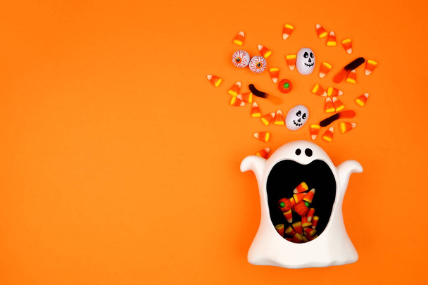 Halloween ghost bowl with spilling candy. Top view on an orange background with copy space. - Photo, Image