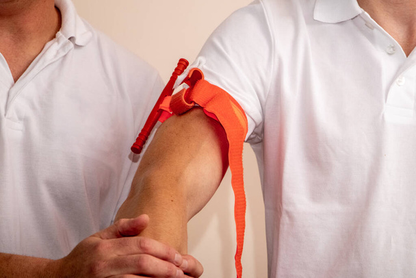 Az egészségügyi szakember bemutatja, hogyan kell érszorítót felhelyezni a karra, hogy sérülés vagy baleset esetén elálljon a vérzés. - Fotó, kép