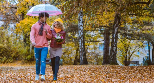 Paar mit unterschiedlichen ethnischen Zugehörigkeiten bei einem Herbstspaziergang im Park voller Herbstfarben - Foto, Bild