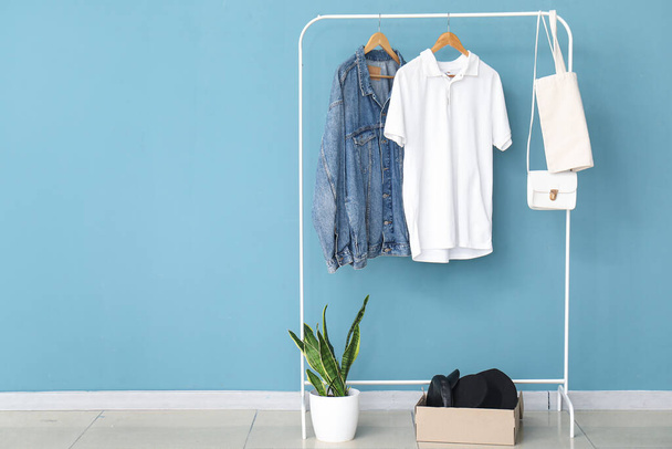 Rack with stylish clothes, accessories and houseplant near color wall - Photo, Image