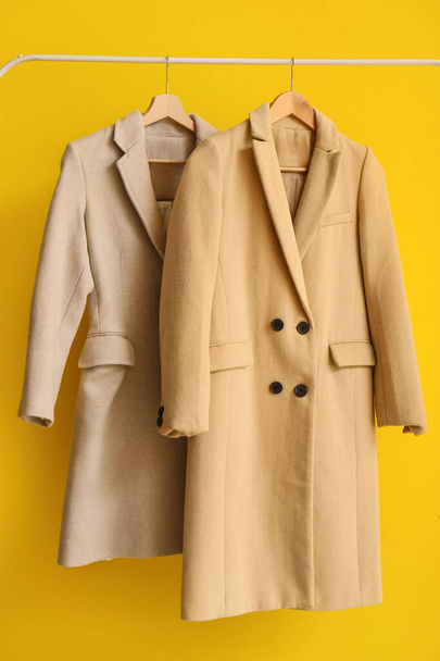 Manteaux élégants suspendus sur support sur fond jaune, gros plan - Photo, image
