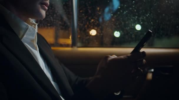Man fingers swiping mobile phone in evening rainy auto close up. Unrecognizable businessman using telephone browsing internet at car backseat. Formal suit boss holding cellphone working luxury vehicle - Footage, Video