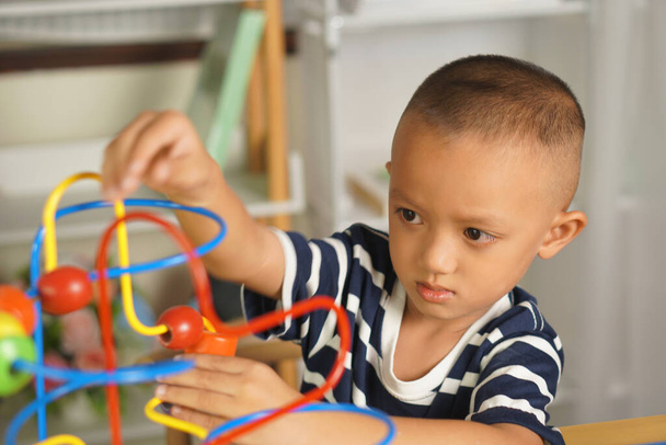Мальчик играет с развивающими игрушками на столе в доме. Путем скольжения мяча по изогнутой стали - Фото, изображение
