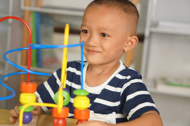 Мальчик играет с развивающими игрушками на столе в доме. Путем скольжения мяча по изогнутой стали - Фото, изображение