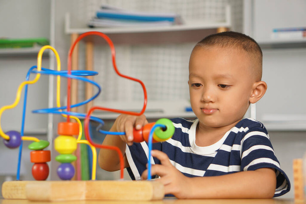 Junge spielt mit Entwicklungsspielzeug auf dem Tisch im Haus. Durch Verschieben der Kugel entlang des gebogenen Stahls - Foto, Bild
