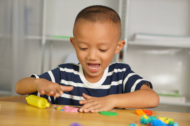 Хлопчик робить пластилін для сприяння розвитку на столі в будинку. Пластилін поставляється в багатьох кольорах, щоб зробити дітей щасливими і веселитися. - Фото, зображення