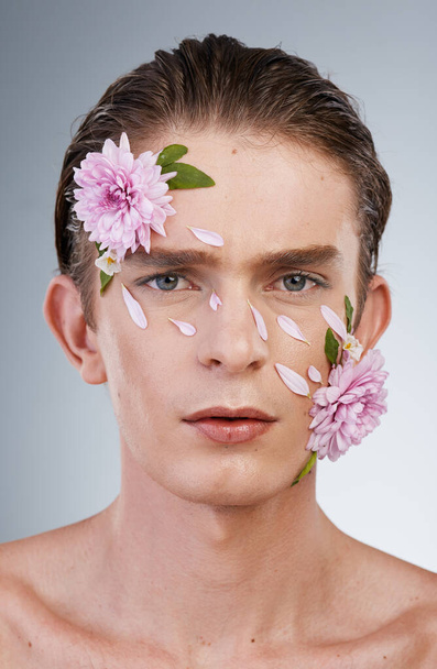 Head, cosmetics and flowers with portrait of man in studio for beauty, natural skincare and creative. Glow, serious and floral with face of model on white background for makeup, spa and wellness. - Photo, Image