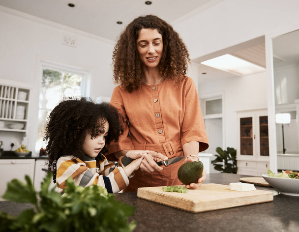 Essen, Avocado und eine Mutter, die mit ihrer Tochter in der Küche ihres Hauses gemeinsam für die Ernährung kocht. Familie, Gesundheit oder Ernährung mit einer Frau, die ihrem Kind beibringt, grünes Gemüse zu essen. - Foto, Bild
