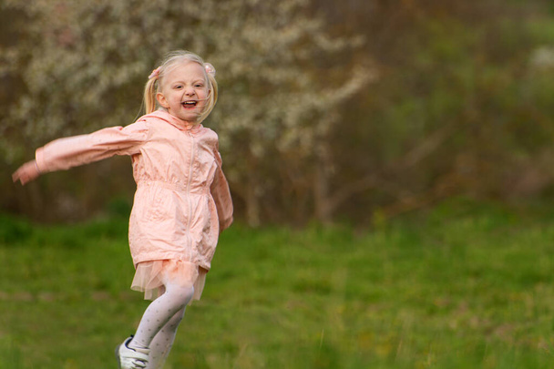 Iloinen naurava valkoihoinen vaaleatukkainen tyttö juoksee pellon poikki. Lapsi tyttö keväällä vihreällä niityllä - Valokuva, kuva