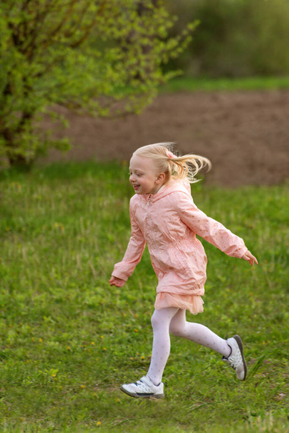 Портрет маленької європейської дівчинки з світлим волоссям у рожевому вбранні, що бігає по полю. Вертикальна рамка - Фото, зображення