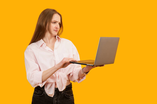 Uštvaná mladá žena držící notebook a práci. Izolované na jasně žlutém pozadí. Kopírovat prostor, makat - Fotografie, Obrázek