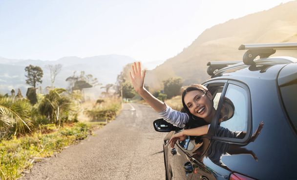 Szczęśliwa piękna młoda kobieta siedząca na przednim siedzeniu samochodu, machająca z okna samochodu i uśmiechnięta. Rodzina, przyjaciele, para podróżująca samochodem na letnie wakacje, cieszący się przyjemnym weekendem, słoneczną pogodą - Zdjęcie, obraz