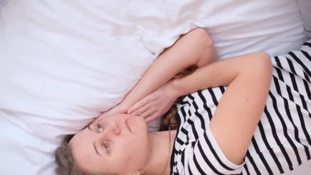 Μια θλιμμένη, αναστατωμένη γυναίκα ξαπλώνει στο κρεβάτι και αποκοιμιέται. Κουρασμένη γυναίκα. Κάθετη βίντεο - Πλάνα, βίντεο