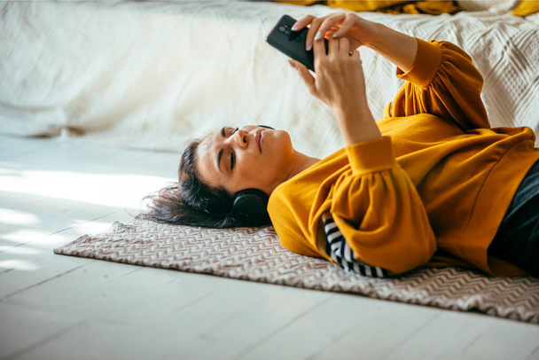 Single woman in her 40s relaxing in her cozy home interior and have leisure time alone with music streaming and online browsing. Autumn lifestyle indoor. - Photo, Image