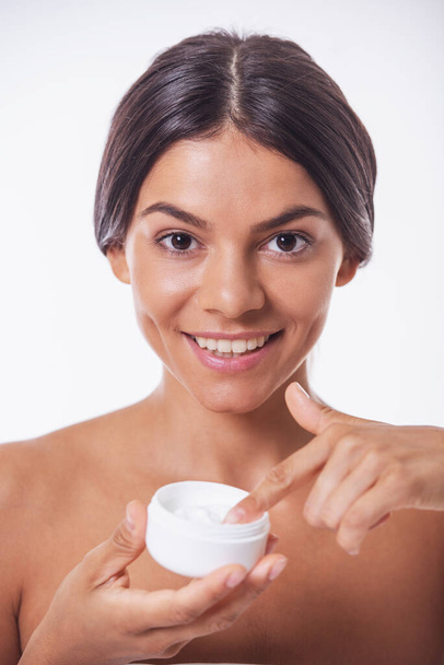Portrait of beautiful girl with bare shoulders holding a jar of cream, looking at camera and smiling, isolated on white - Photo, Image