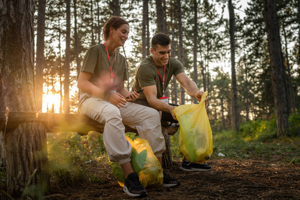Paar oder Teenager Freunde gen Z männlich und weiblich kaukasischen Mann Frau sammeln Müll Plastikflaschen und Papier aus dem Wald Säuberung der Natur an sonnigen Tag Umweltpflege Ökologie-Konzept - Foto, Bild