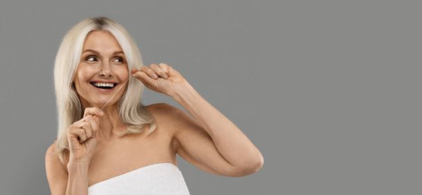Happy Mature Beautiful Woman Cleaning Teeth With Dental Floss And Looking Aside At Copy Space, Smiling Senior Female With Beautiful Smile Standing Isolated Over Grey Studio Background, Panorama - Valokuva, kuva