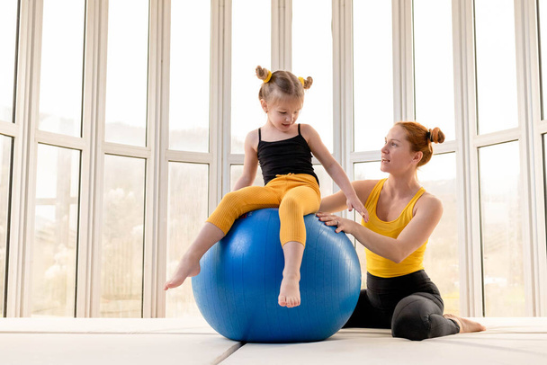 Young fit mom and her daughter having fun with fitness ball in a gym - Фото, зображення