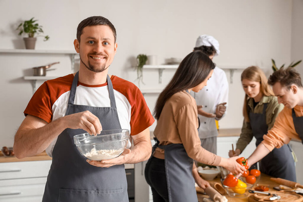 Молодий чоловік з мискою з борошна під час приготування їжі на кухні - Фото, зображення