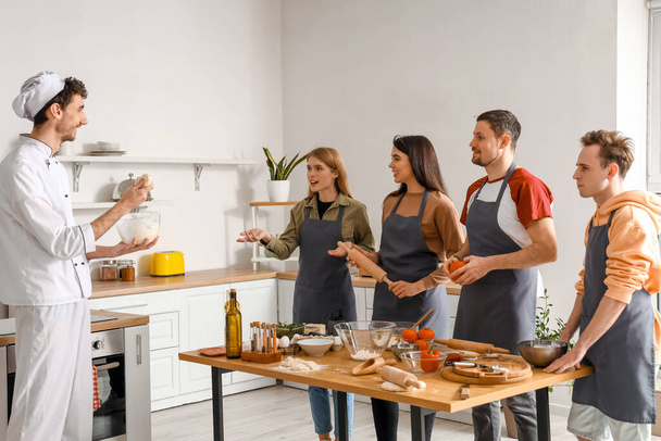 Groep jongeren met Italiaanse chef-kok bereidt pizza tijdens kookles in keuken - Foto, afbeelding