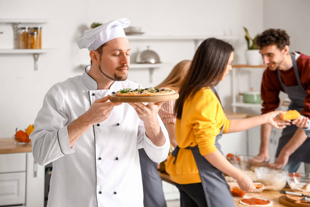Ιταλός σεφ με έτοιμη πίτσα κατά τη διάρκεια του μαθήματος μαγειρικής στην κουζίνα - Φωτογραφία, εικόνα