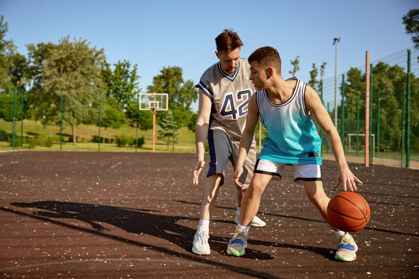 Joven entrenador enseñando a un adolescente a jugar baloncesto en la cancha callejera. Clase de deporte para chicos adolescentes - Foto, imagen