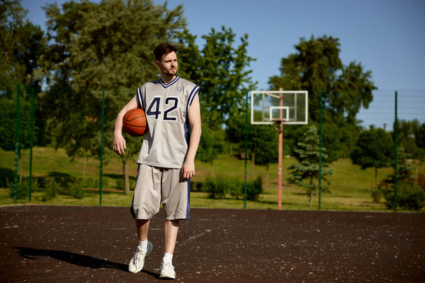 Serious joven jugador de baloncesto caminando con pelota después del entrenamiento deportivo en la cancha de calle retrato de cuerpo entero - Foto, Imagen