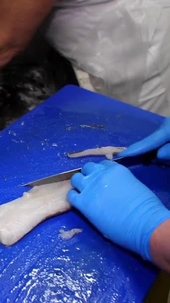 Vídeo vertical. Las manos de un cocinero con guantes en una tabla de cortar cortan la columna vertebral y las aletas de un filete de pescado de mar con un cuchillo. Cocinar comidas. - Imágenes, Vídeo