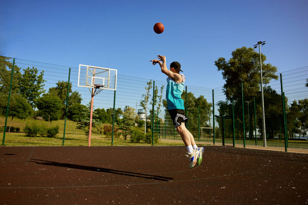 Ragazzo adolescente attivo che gioca a basket sul campo all'aperto di strada. Giovane ragazzo che salta con palla puntando cerchio - Foto, immagini