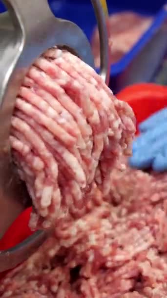 Vertical video. Minced pork and veal comes out of the holes of the meat grinder and falls into an iron bowl. The cooks hands fix the products. Production of meat cutlets and burgers. - Footage, Video