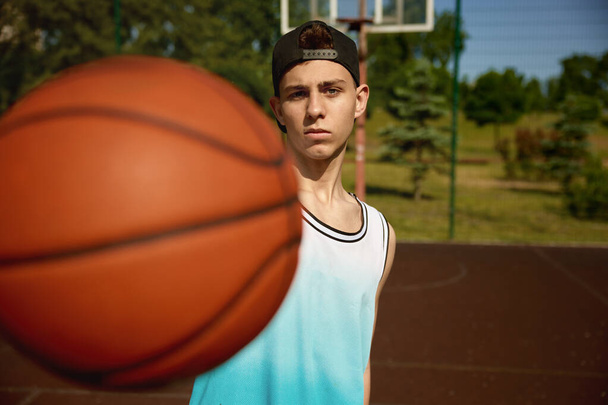 カメラのボールフロントを保持するティーンエイジャーのバスケットボール選手のクローズアップショット. スポーツ活動と若者 - 写真・画像