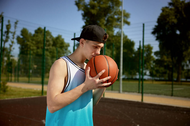 Teenager-Basketballspieler küsst Ball und betet für ein Tor und demonstriert gute Beziehung zum Lieblingssport - Foto, Bild