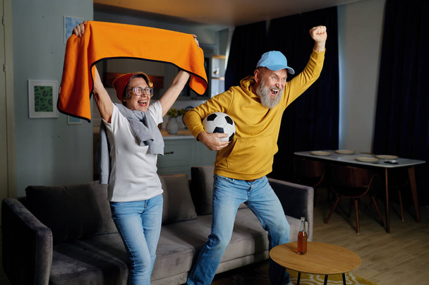 Glückliches Seniorenpaar jubelt vor dem Fernseher bei Sportwettkämpfen. Ältere Fußballfans feiern Sieg der Lieblingsmannschaft - Foto, Bild