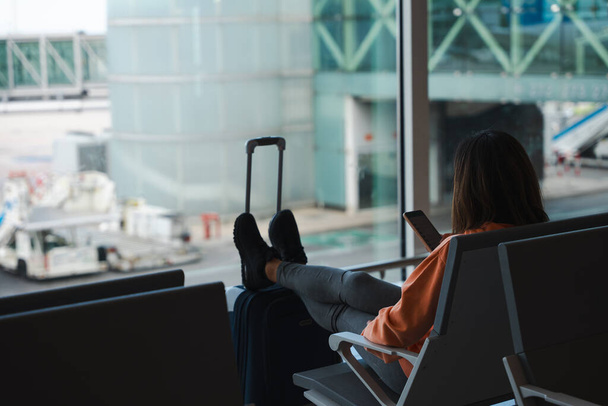 Frau checkt ihr Handy beim Warten auf ihren Flug am Flughafen. - Foto, Bild