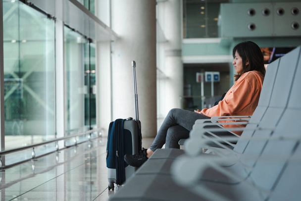 座っている女性は,空港の窓から見て,彼女の飛行を待っています. - 写真・画像