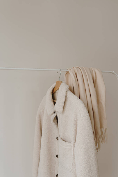 白い暖かいウールの秋の季節のジャケットおよび白い壁の上のハンガーのスカート. ミニマリストファッション服ワードローブ - 写真・画像