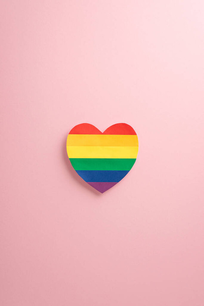 Погрузитесь в празднование месяца ЛГБТК + Гордость. Посмотрите на завораживающий вертикальный снимок сверху вниз, демонстрирующий флаг ЛГБТК + на форме сердца на мягком розовом фоне пастели. Удобная реклама с предоставлением места для копирования - Фото, изображение