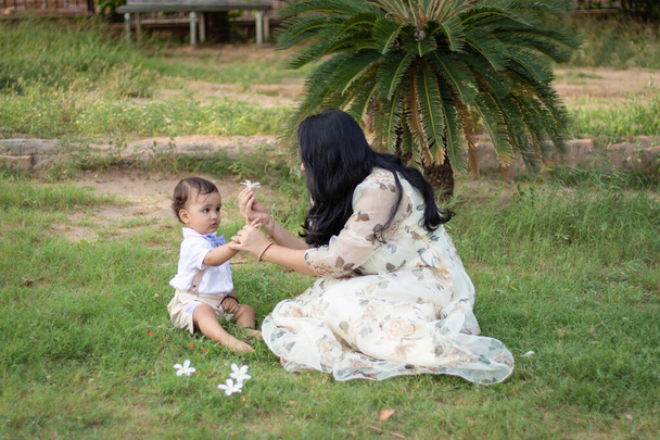 madre dando flor a lindo bebé niño y disfrutando el uno del otro al aire libre - Foto, Imagen