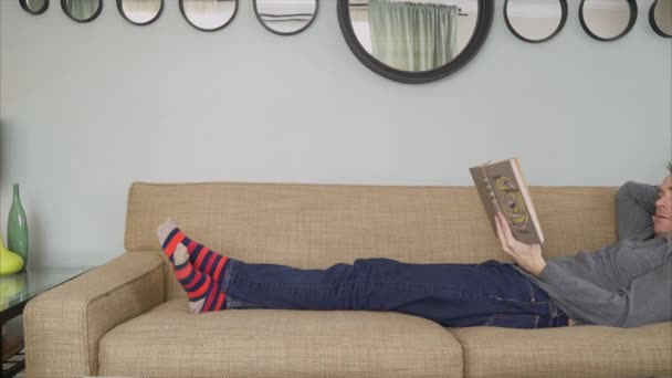 Muž čtení knih v útulném obývacím pokoji ve 4k - Záběry, video