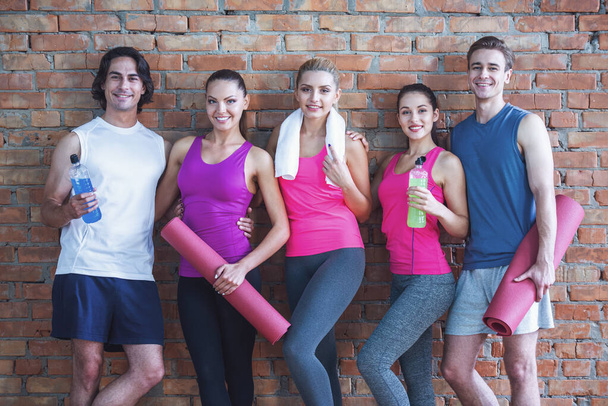 Beautiful sports people are holding sports equipment, looking at camera and smiling, on brick wall background - Photo, Image