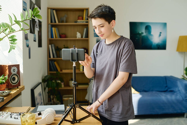 Bruneta žena teenager dotýkání obrazovky smartphone na stativ při přípravě na natáčení nového videa nebo natáčení livestream doma - Fotografie, Obrázek