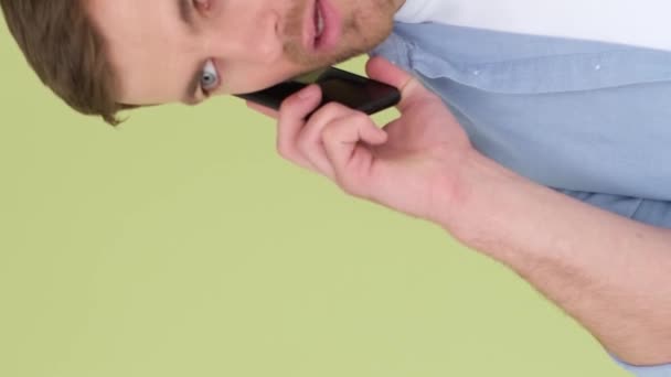 Agresivní muž mluví na smartphonu a křičí nespokojeně, izolovaný na pozadí ve studiu. Chlápek s nervovým zhroucením. Svislé video - Záběry, video